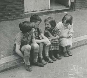 876879 Afbeelding van twee jongens en twee meisjes zittend op een stoeprand in een onbekende straat in Wijk C te ...